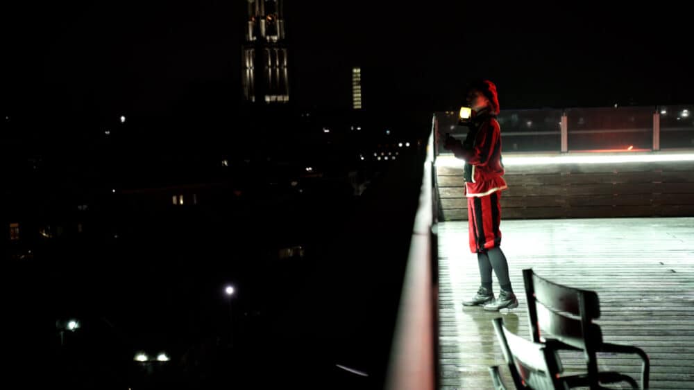 Piet staat in het donker op een hoog dakterras over de stad uit te kijken